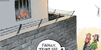 Donald Trump looks out the window of a prison, surrounded by a barbed-wire topped wall. Two people stand outside, saying "Finally, Trump has his wall."